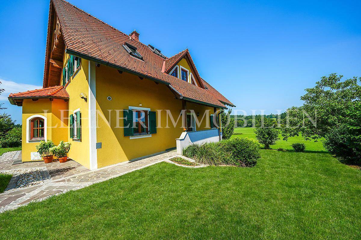 Seitenansicht des Hauses mit gelber Fassade, grünem Rasen und Blick auf die umliegende Landschaft.