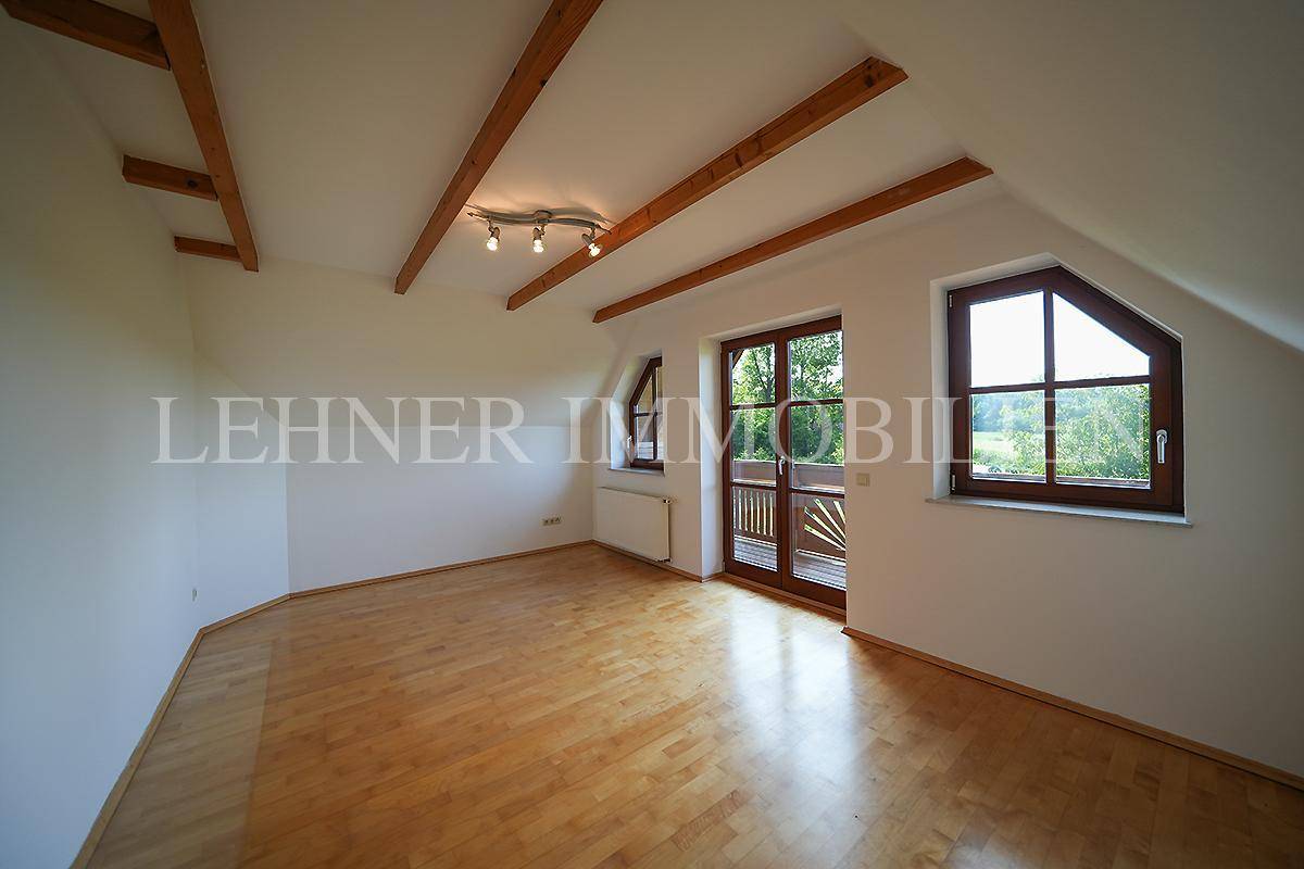 Helles Schlafzimmer im Dachgeschoss mit Holzboden, sichtbaren Balken und Balkonzugang.