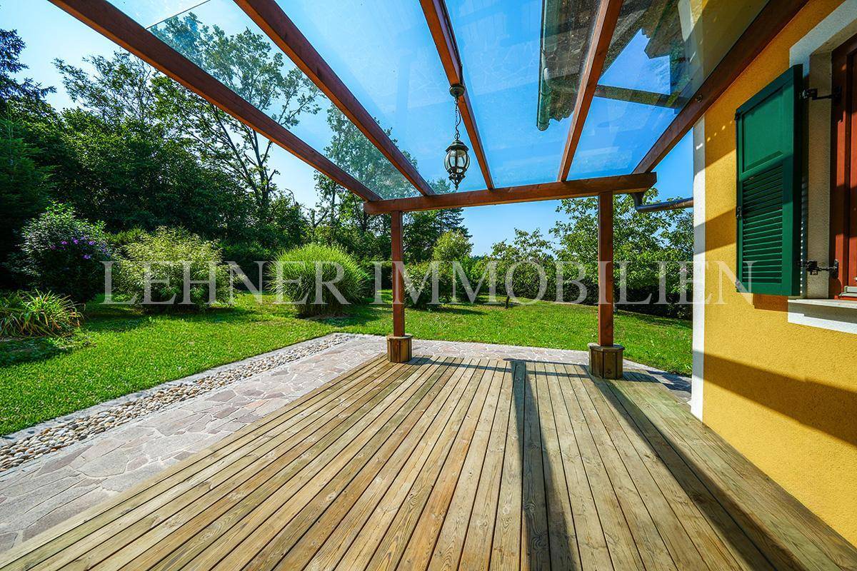 Überdachte Holzterrasse mit Glasdach und Blick auf den weitläufigen Garten.