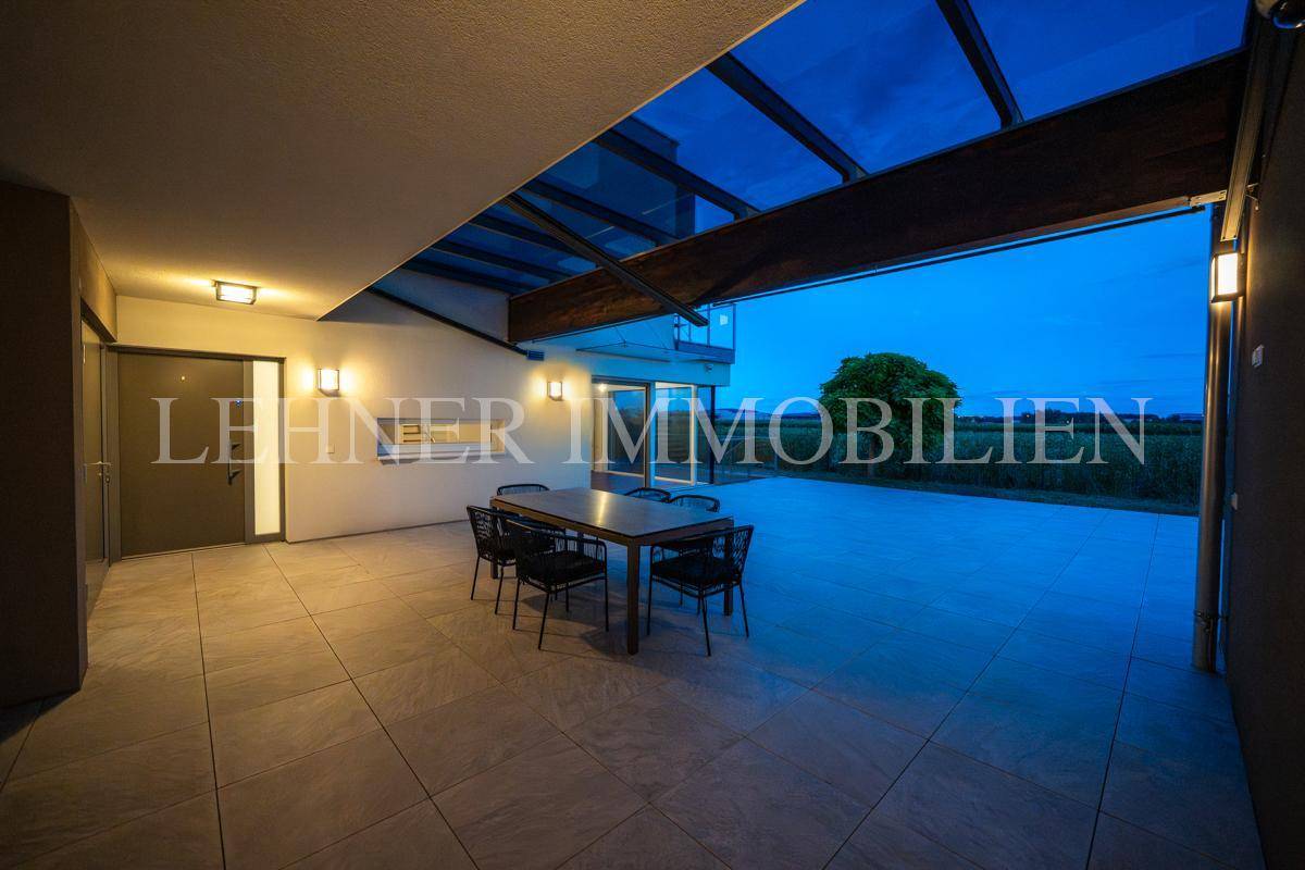 Überdachte Terrasse bei Nacht mit Essbereich und beleuchtetem Eingang, der zum Haus führt.