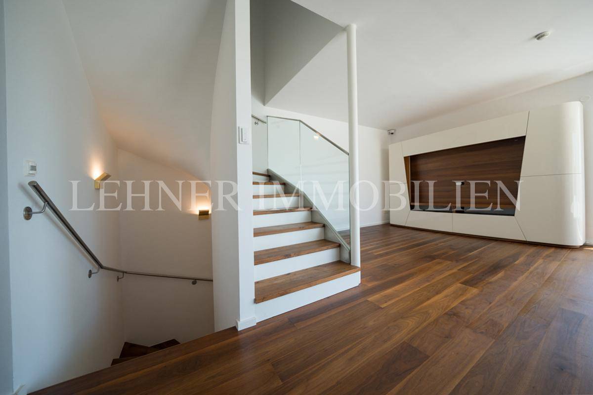 Moderne Holztreppe mit Glasgeländer, die in die untere Etage führt, neben einer stilvollen Wandverkleidung.