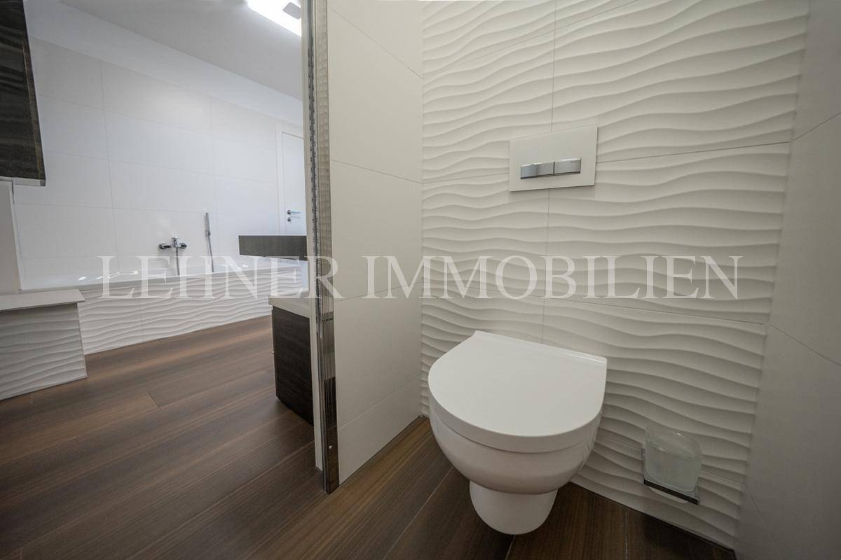 Modernes WC mit wandmontierter Toilette und stilvollen Wellenfliesen an der Wand.