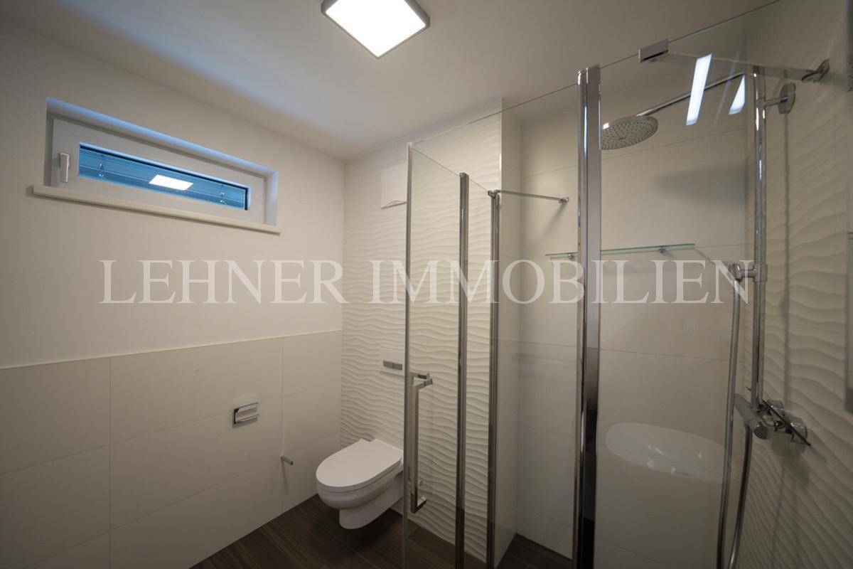 Funktionales Badezimmer mit Duschbereich, WC und kleinem Fenster für natürliche Belüftung.