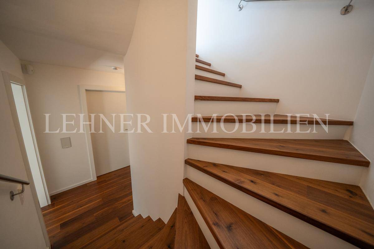Treppenaufgang mit eleganten Holzstufen und modernem Design, führt zu den oberen Etagen.