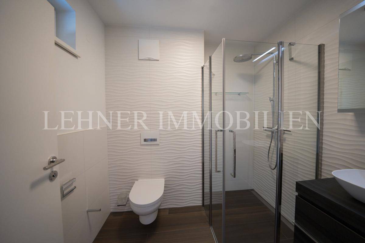 Helles Badezimmer mit moderner Duschkabine, wandhängendem WC und eleganten Wandfliesen.