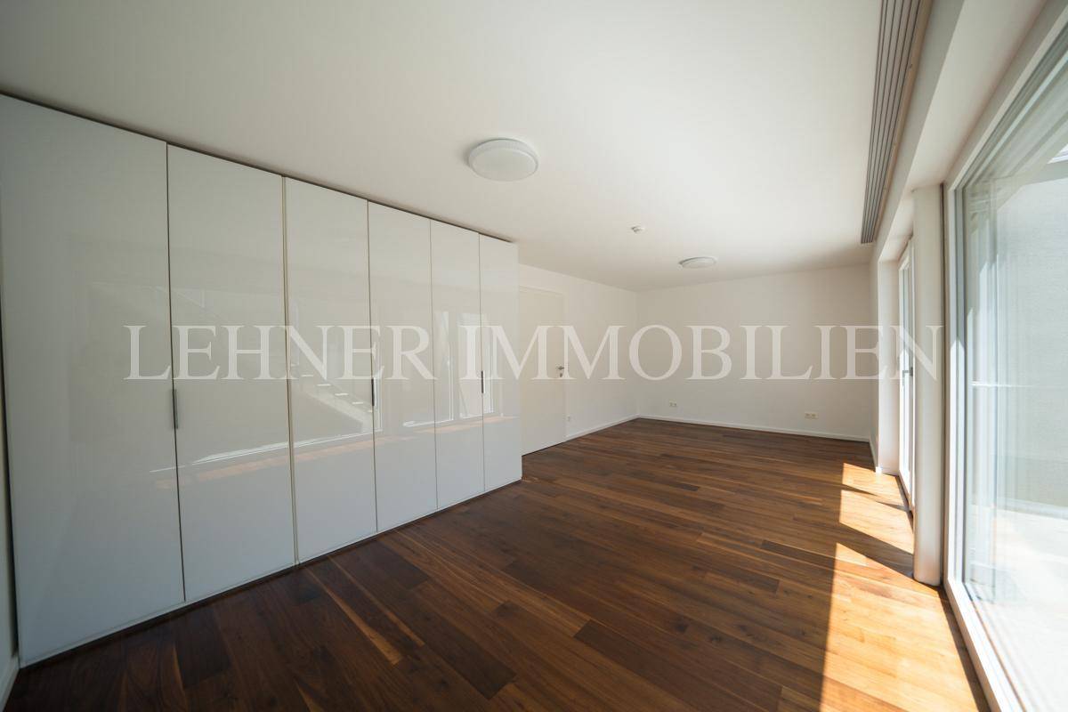 Helles Zimmer mit eleganten weißen Einbauschränken und hochwertigem Holzfußboden.