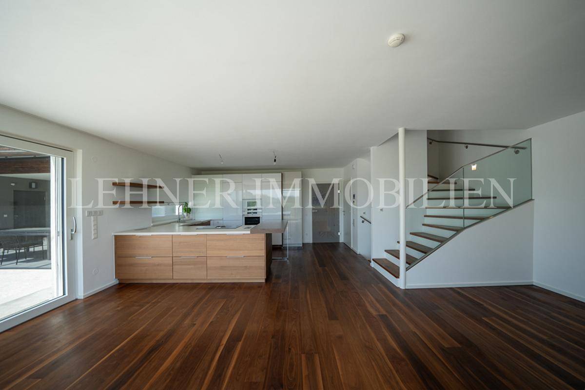 Offener Wohnbereich mit moderner Küche, Holzboden und eleganter Treppe zum Obergeschoss.