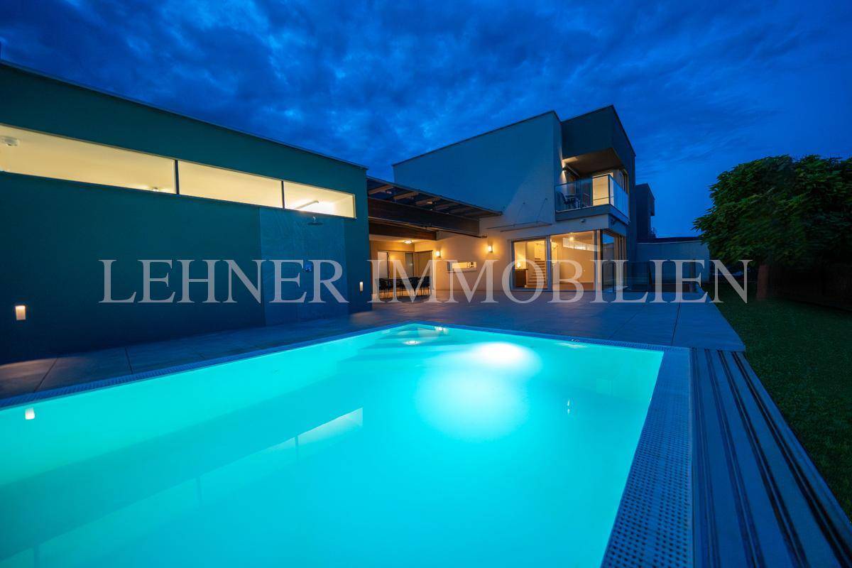 Beleuchtete moderne Villa bei Nacht mit leuchtendem Pool und einladender Terrasse.