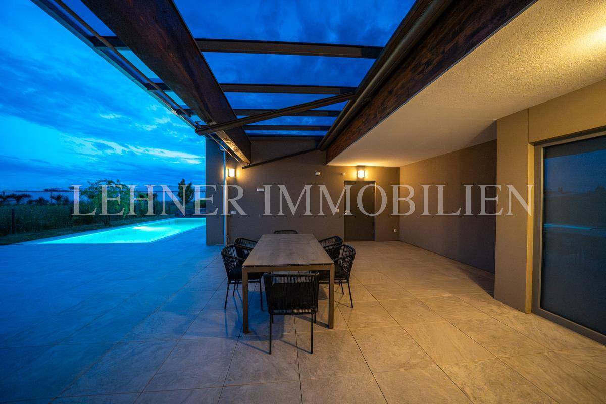 Beleuchtete überdachte Terrasse bei Nacht mit Essbereich und Blick auf den schimmernden Pool.