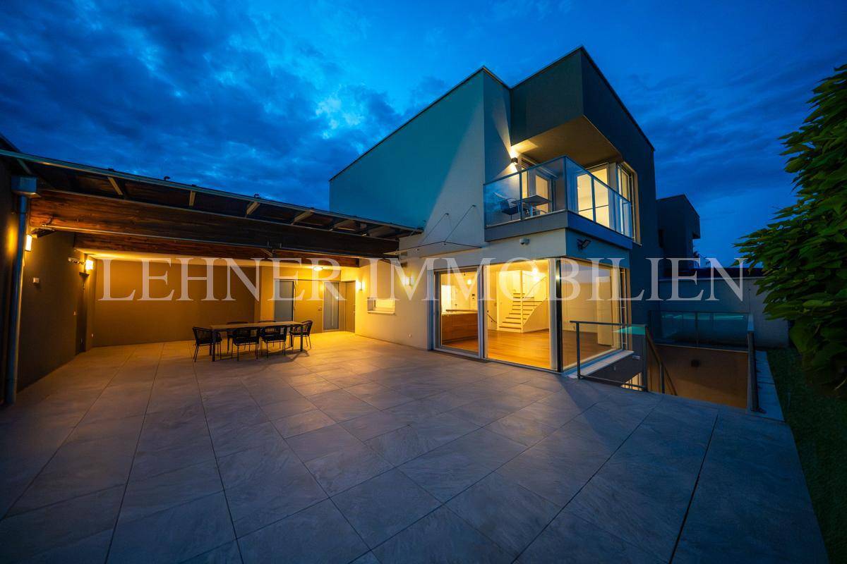 Moderne Villa bei Nacht mit beleuchteten Innenräumen und einer großzügigen Terrasse.