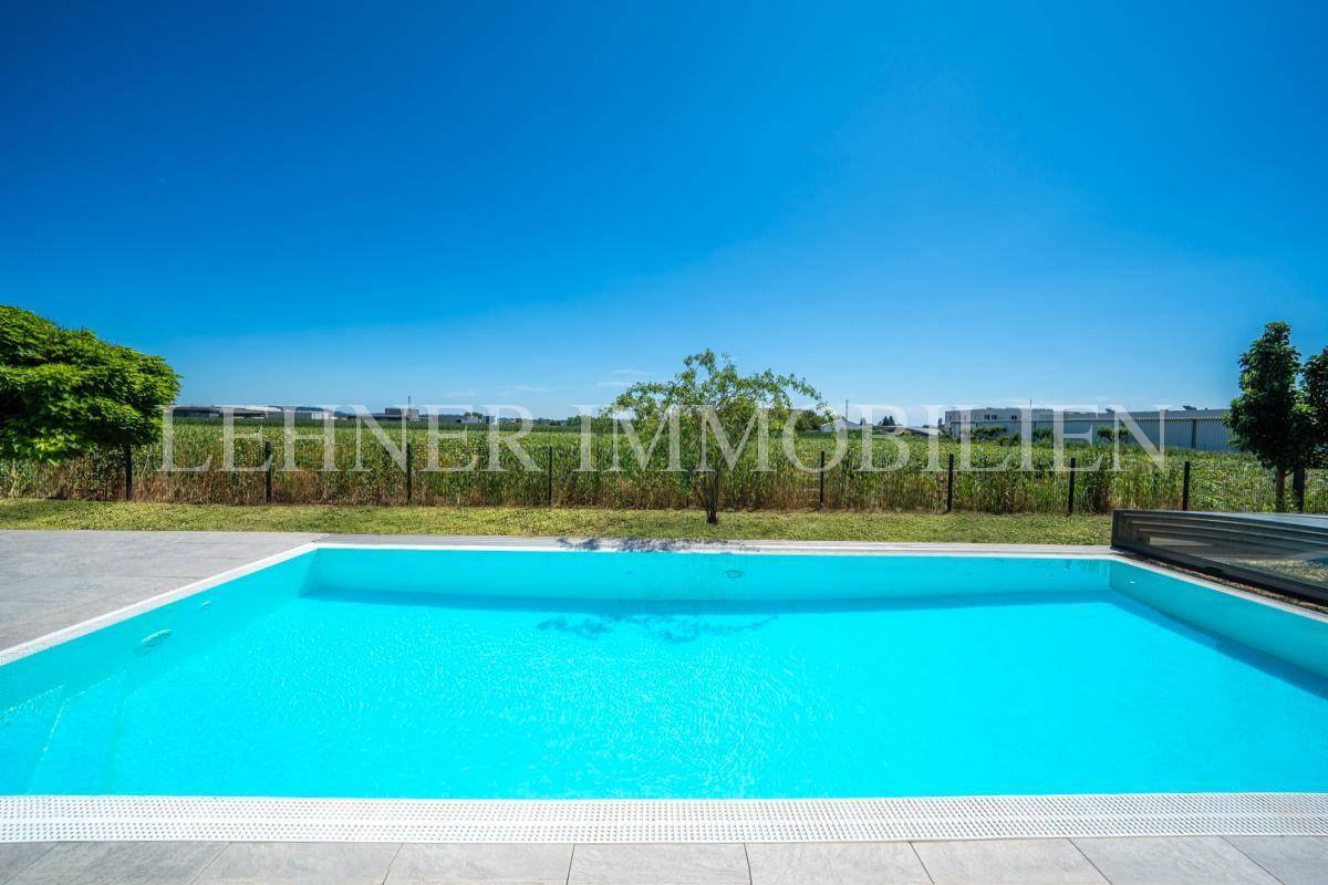 Großer Pool mit Blick auf weite Felder und die ländliche Umgebung unter strahlend blauem Himmel.
