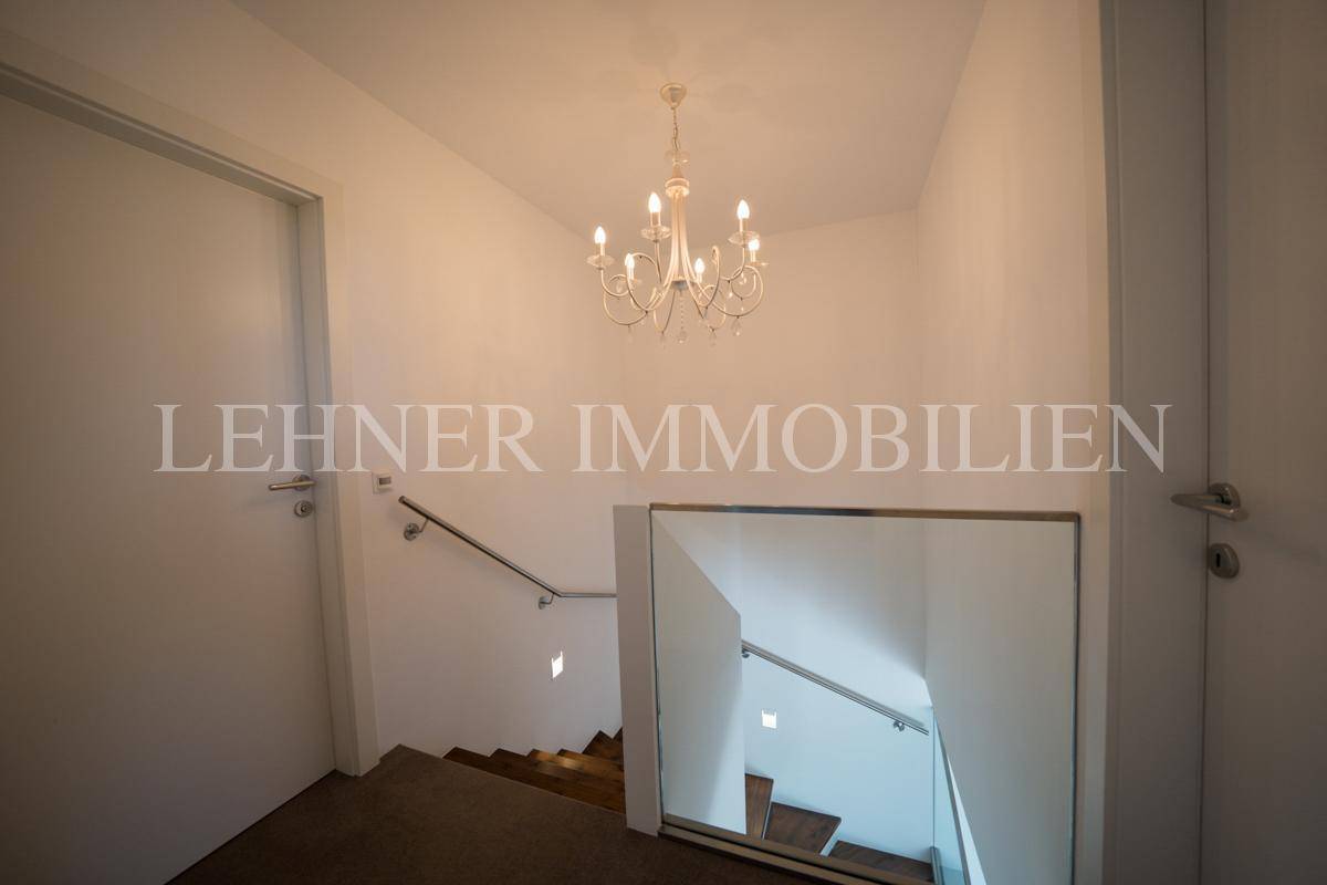 Treppenhaus mit Holzstufen, Glasgeländer und klassischem Kronleuchter, der den Bereich erhellt.