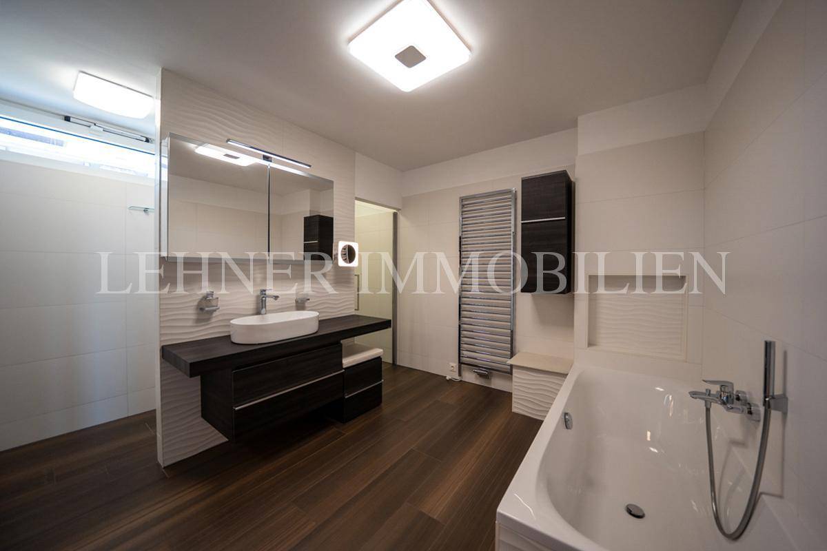 Modernes Badezimmer mit dunklem Holzfußboden, Badewanne, Einzelwaschbecken und Duschbereich.
