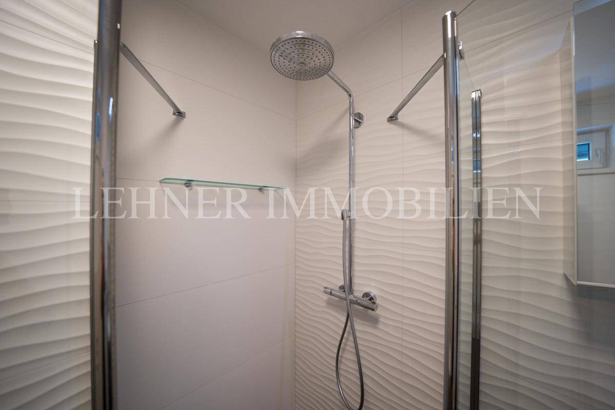 Detailansicht der modernen Duschkabine mit Regenduschkopf und Glasabtrennung.