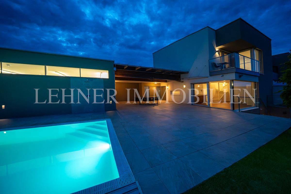 Stimmungsvolle Nachtansicht der Villa mit beleuchtetem Pool und großzügiger Terrasse unter dunklem Himmel.