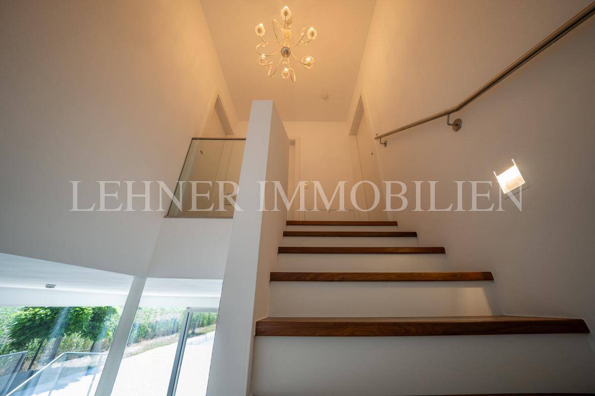 Heller Treppenaufgang mit modernen Holzstufen, Glasgeländer und eleganter Deckenleuchte.