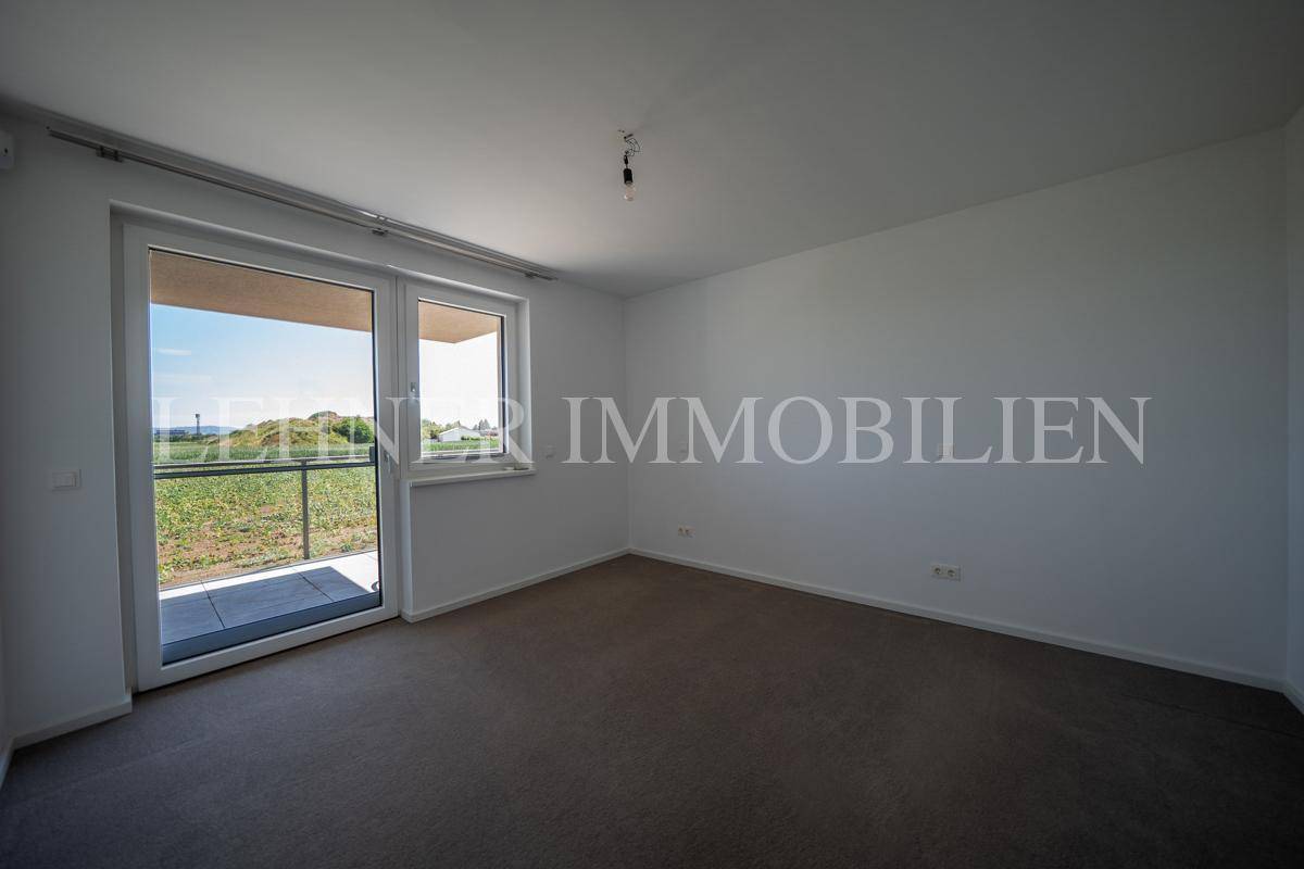 Helles Zimmer mit Teppichboden und Zugang zu einem Balkon mit weitem Blick ins Grüne.