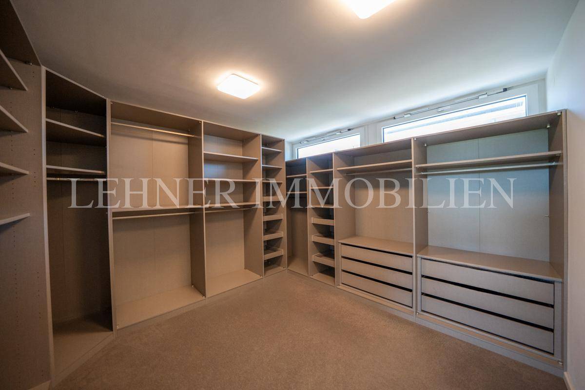 Heller begehbarer Kleiderschrank mit maßgefertigten Regalen und Fenstern für Tageslicht.