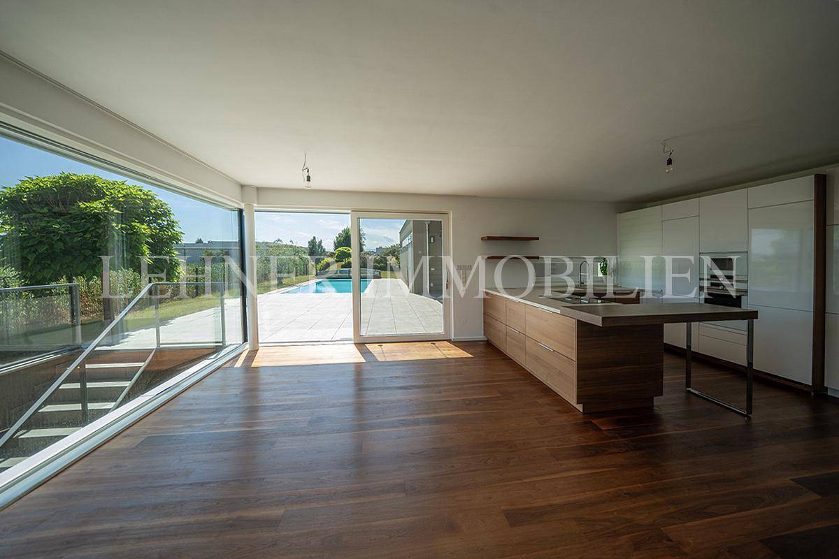 Helle, offene Küche mit Holzfronten, Kochinsel und großen Fenstern mit Blick auf den Außenbereich.