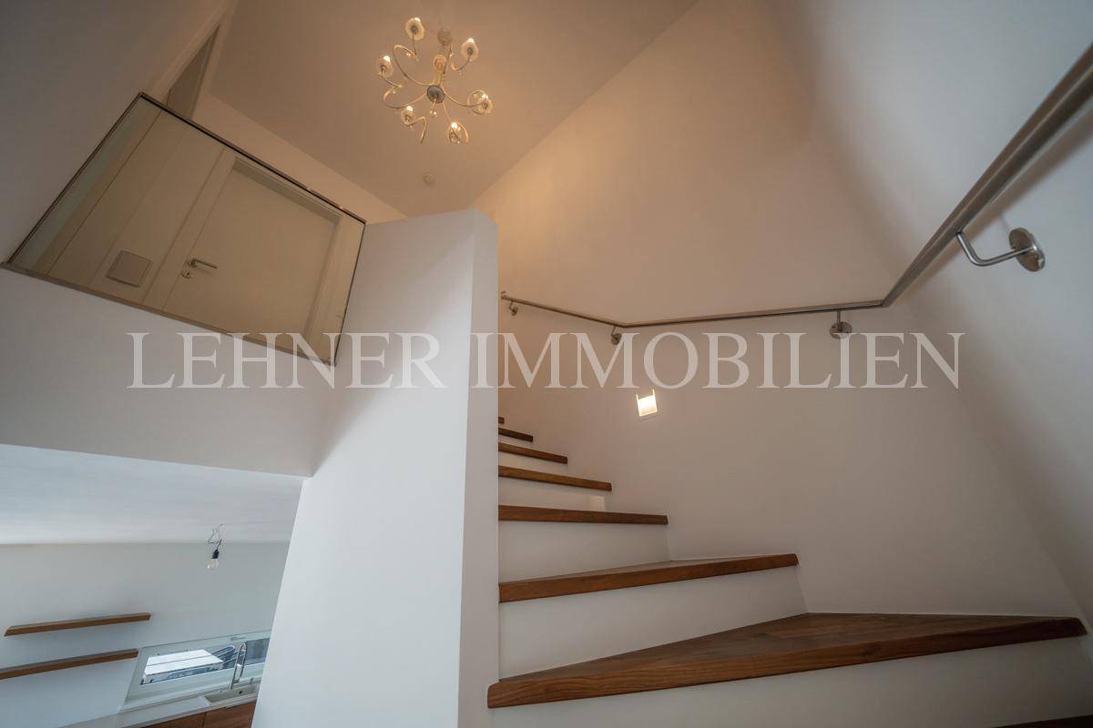 Moderner Treppenaufgang mit Holzstufen, Glasgeländer und stilvoller Deckenbeleuchtung.