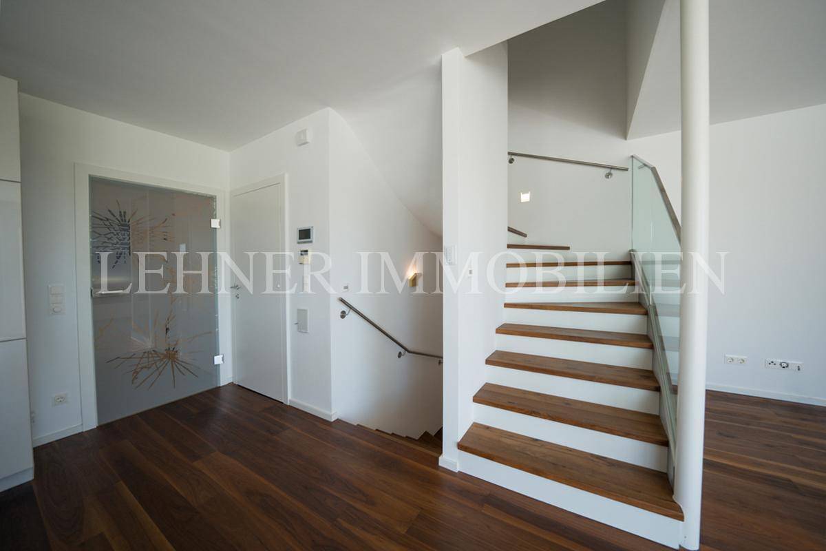 Moderner Eingangsbereich mit Holztreppe, Glasgeländer und stilvoller Glastür.