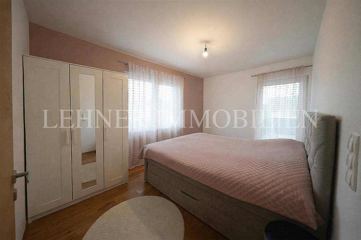 Schlafzimmer mit Holzboden, großem Bett und einem weißen Kleiderschrank mit Spiegeltüren.