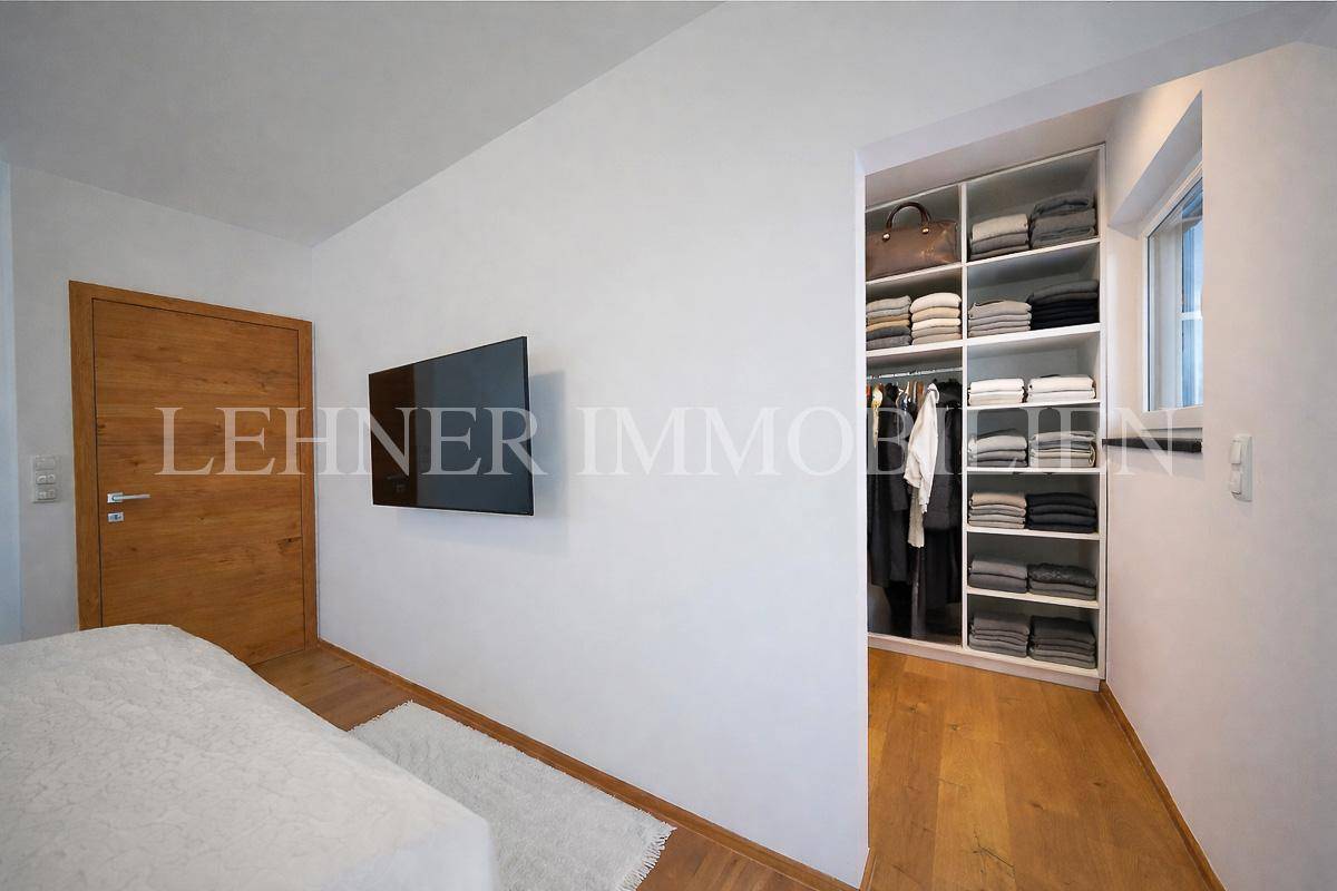 Schlafzimmer mit Holzboden, an der Wand montiertem Fernseher und Zugang zum begehbaren Kleiderschrank.