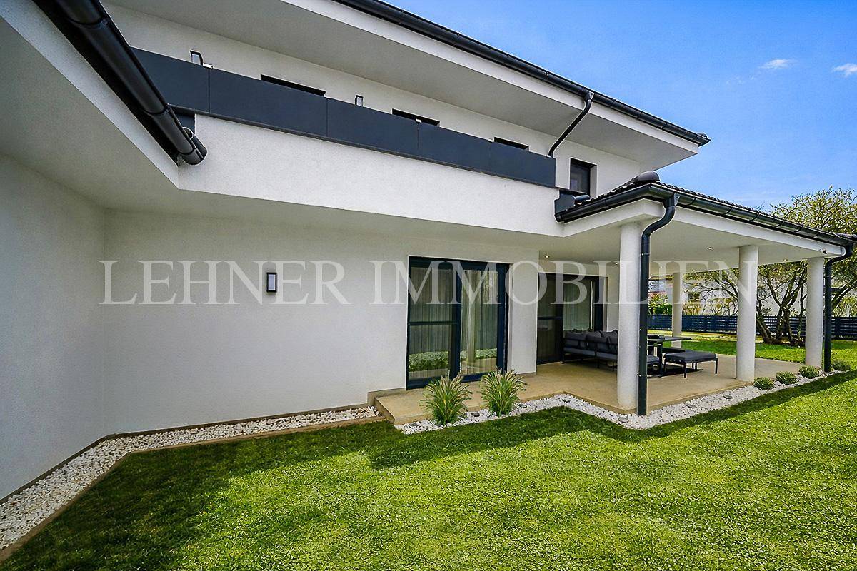 Seitlicher Blick auf das moderne Haus mit überdachter Terrasse und Zugang zum Garten.