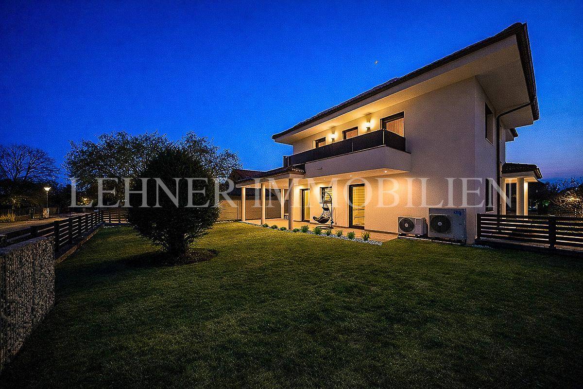 Garten und Rückseite des Hauses bei Nacht mit sanfter Beleuchtung und Rasenfläche.