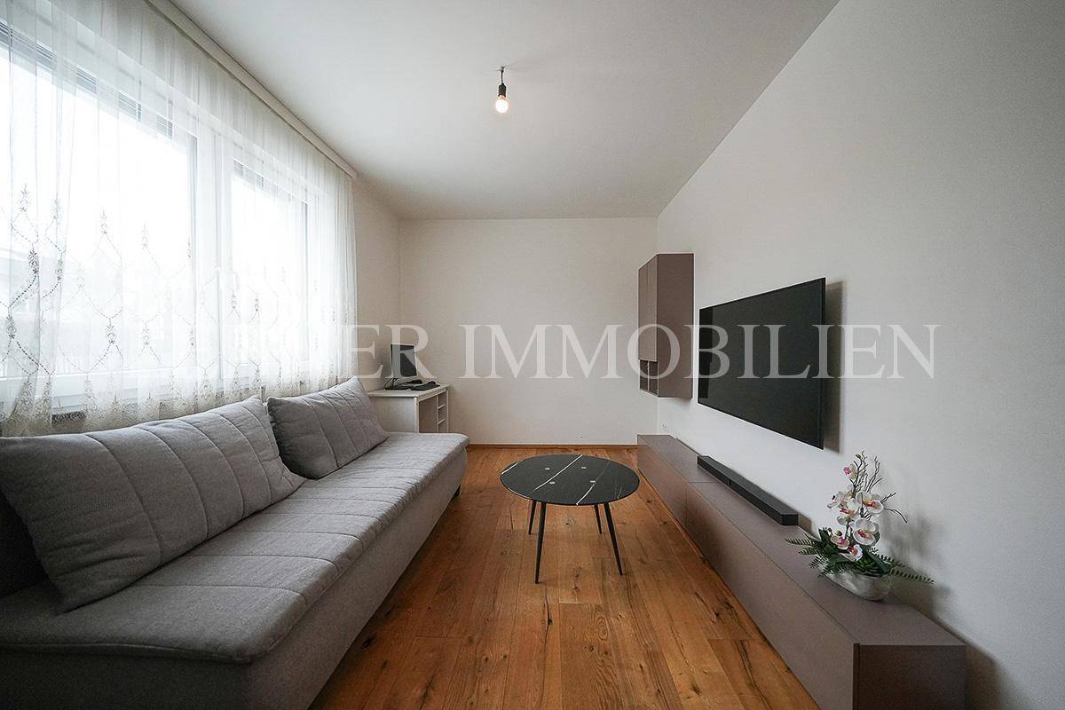 Gemütliches Zimmer mit Holzboden, großem Fenster und Sofa.