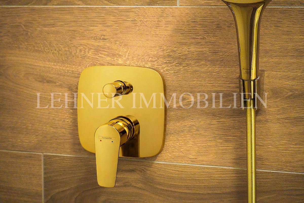 Goldene Duscharmaturen in einem eleganten Badezimmer mit Holzoptik-Fliesen.