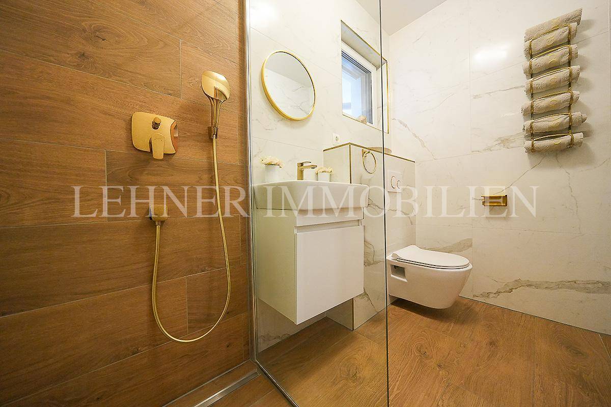 Modernes Badezimmer mit begehbarer Dusche, Marmorfliesen und goldenen Armaturen.