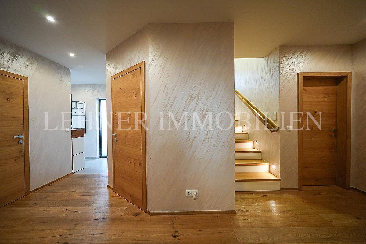 Heller Flur mit Holzboden, strukturierten Wänden und Treppenaufgang.