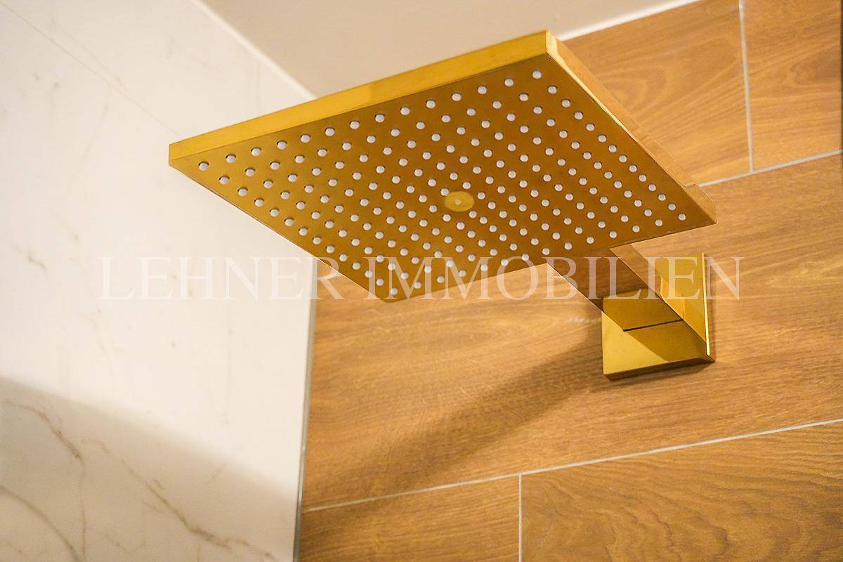 Goldene Regendusche in einem luxuriösen Badezimmer mit Holz- und Marmorfliesen.