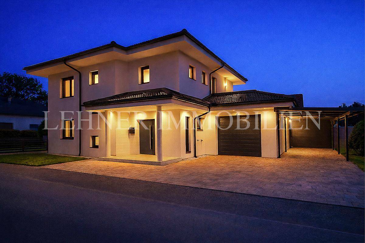 Modernes Haus bei Nacht mit stimmungsvoller Beleuchtung, Garage und Carport.