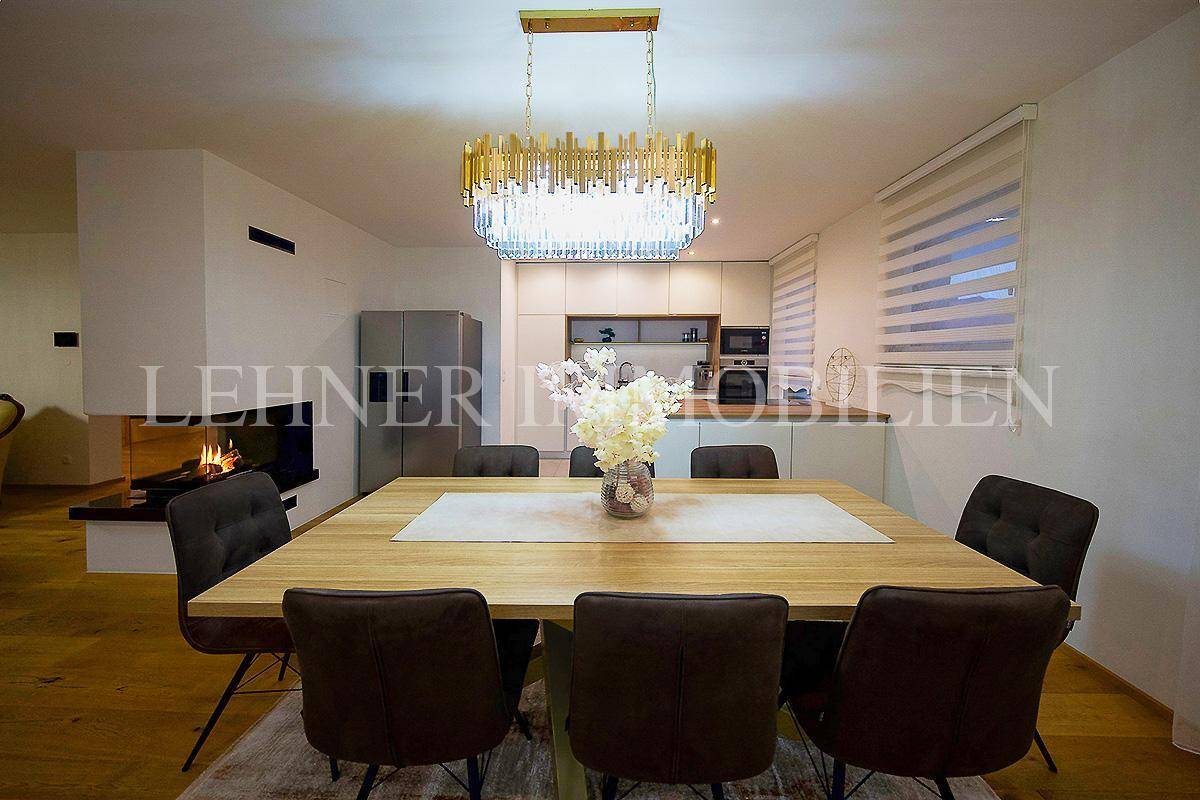 Eleganter Essbereich mit großem Holztisch, bequemen Stühlen und einem modernen Kronleuchter.