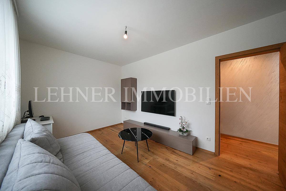 Helles Zimmer mit Holzboden, Fernseher und Zugang zu einem weiteren Raum.
