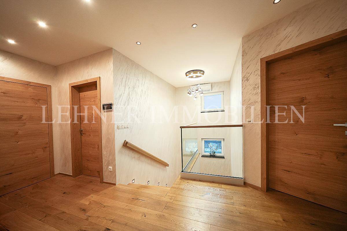 Heller Flur mit Holzfußboden, modernen Türen und Blick auf das Treppenhaus mit Glasgeländer.
