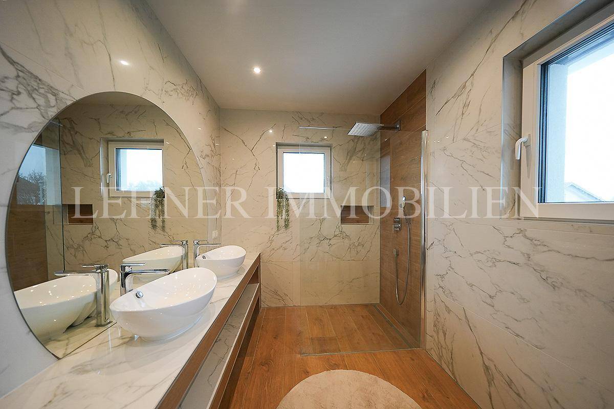 Großes Badezimmer mit Doppelwaschbecken, begehbarer Dusche und zwei Fenstern für Tageslicht.