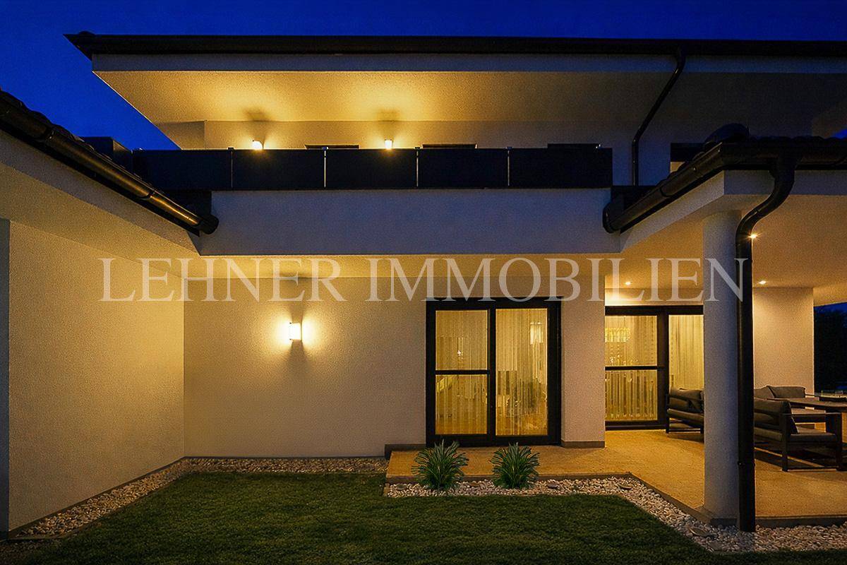 Beleuchteter Terrassenbereich und Balkon des modernen Hauses bei Nacht.