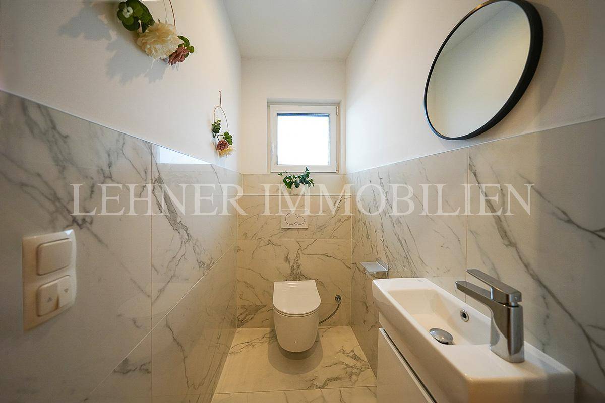 Modernes Gäste-WC mit Marmorfliesen, wandhängendem WC und einem kleinen Waschbecken.