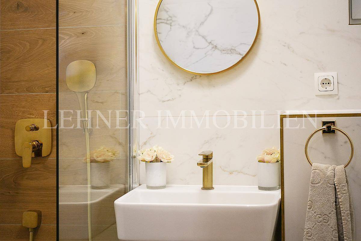 Detailansicht des Waschbeckens mit goldenem Wasserhahn und rundem Spiegel im modernen Bad.