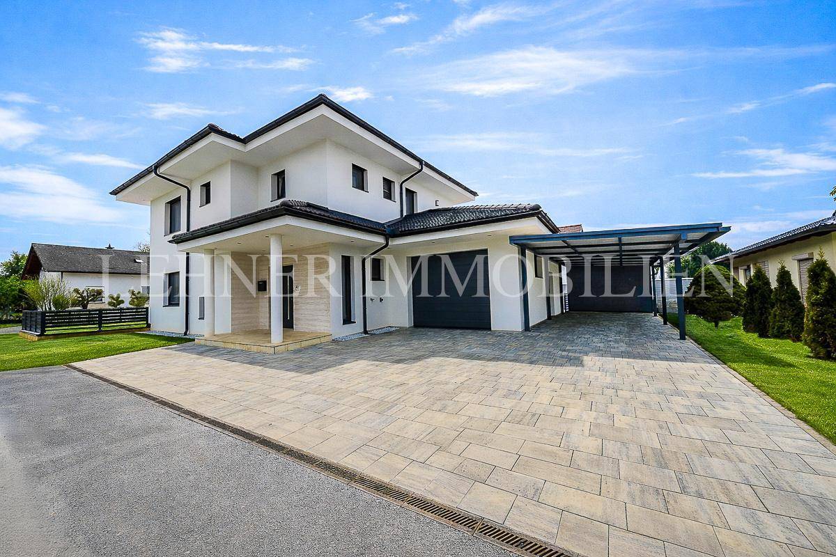Modernes Einfamilienhaus mit Garage, Carport und großzügiger gepflasterter Auffahrt.