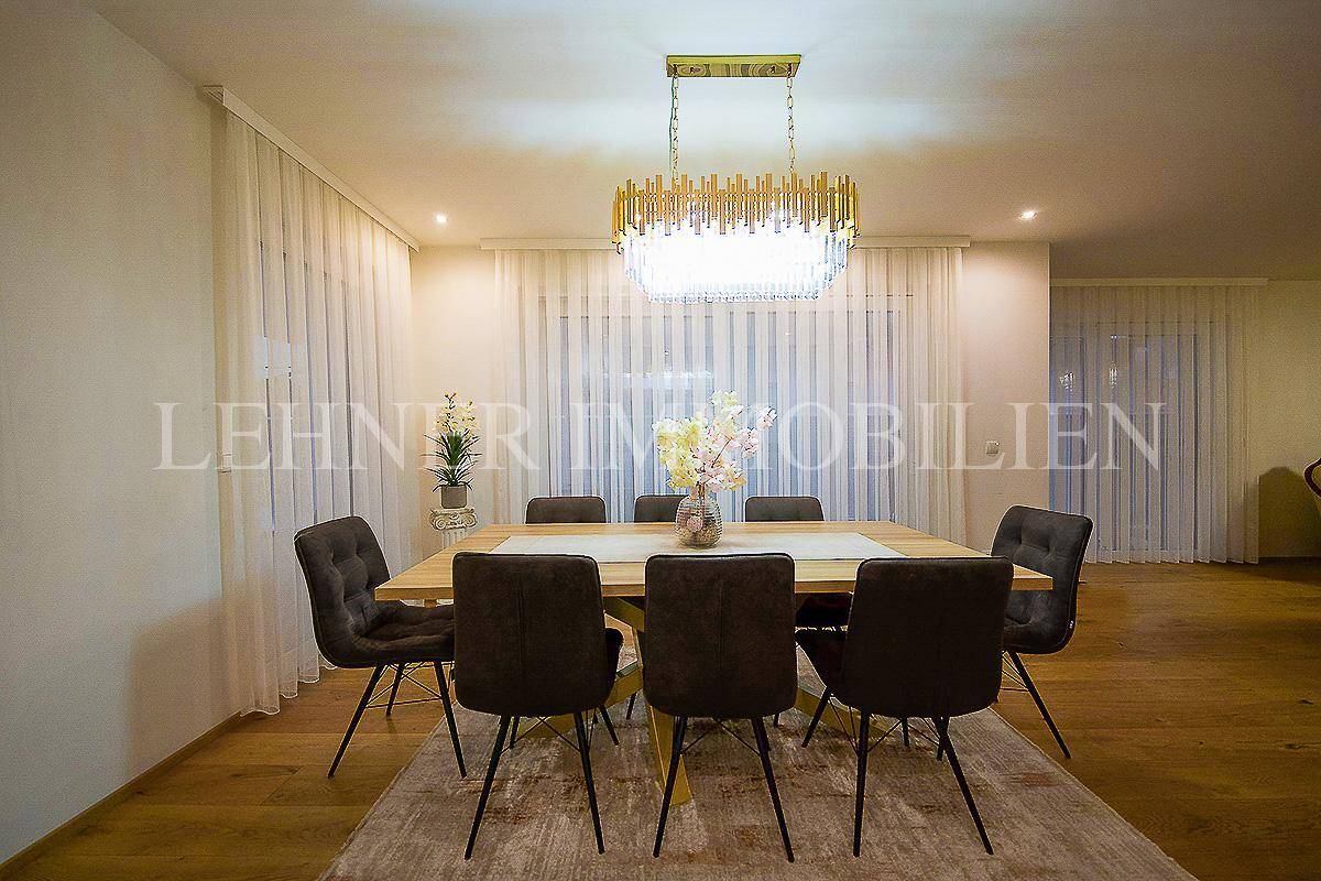 Eleganter Essbereich mit großem Holztisch, bequemen Stühlen und moderner Beleuchtung.