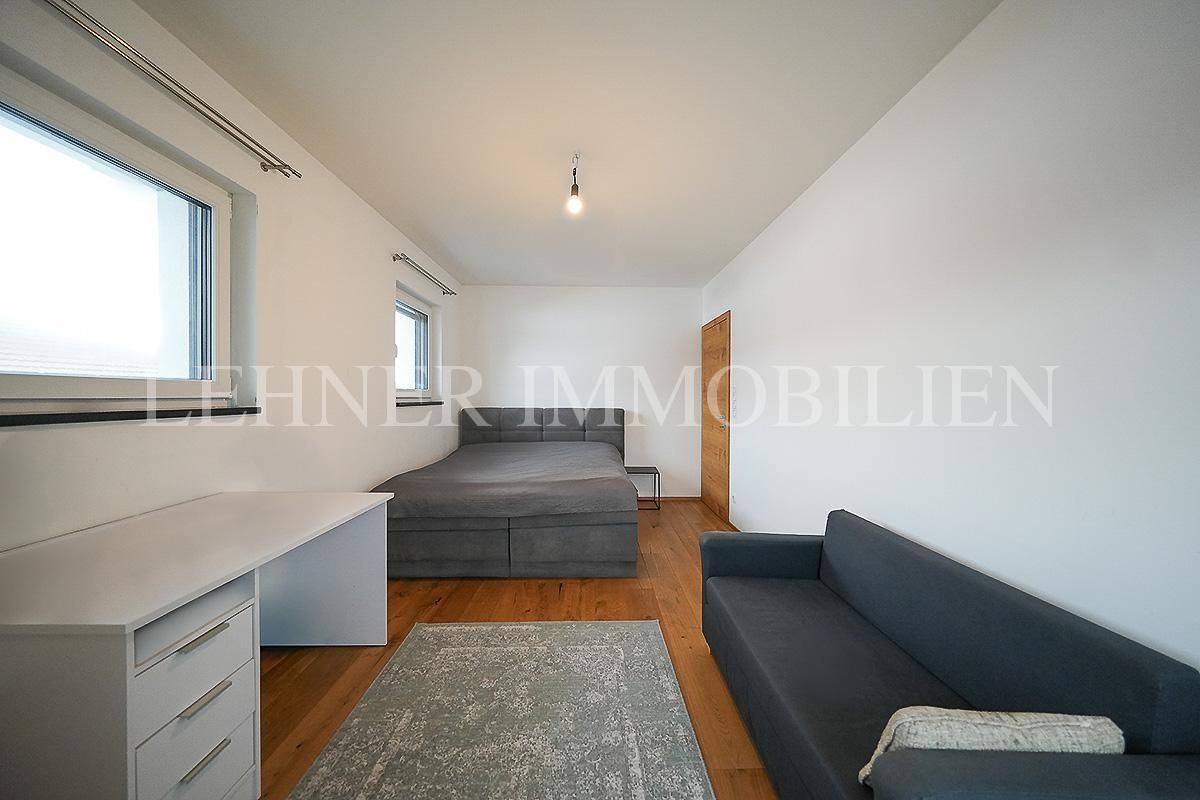 Geräumiges Schlafzimmer mit Holzboden, Sofa und Schreibtisch, ideal als Jugendzimmer.