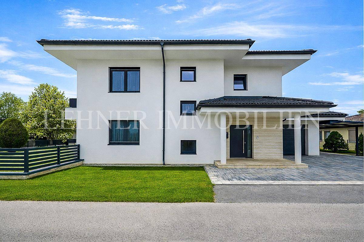 Moderne weiße Hausfassade mit dunklen Fenstern und gepflegtem Vorgarten.