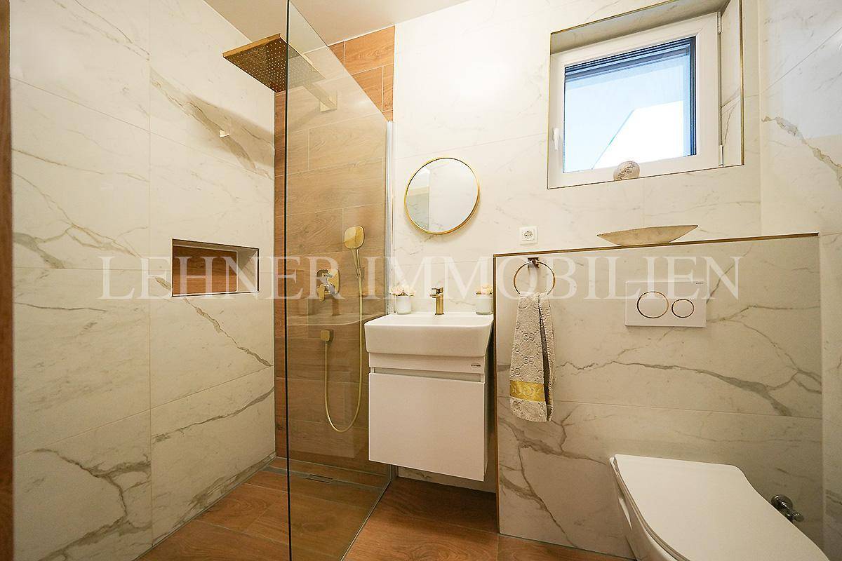 Elegantes Badezimmer mit begehbarer Dusche, Marmorfliesen und goldenen Details.