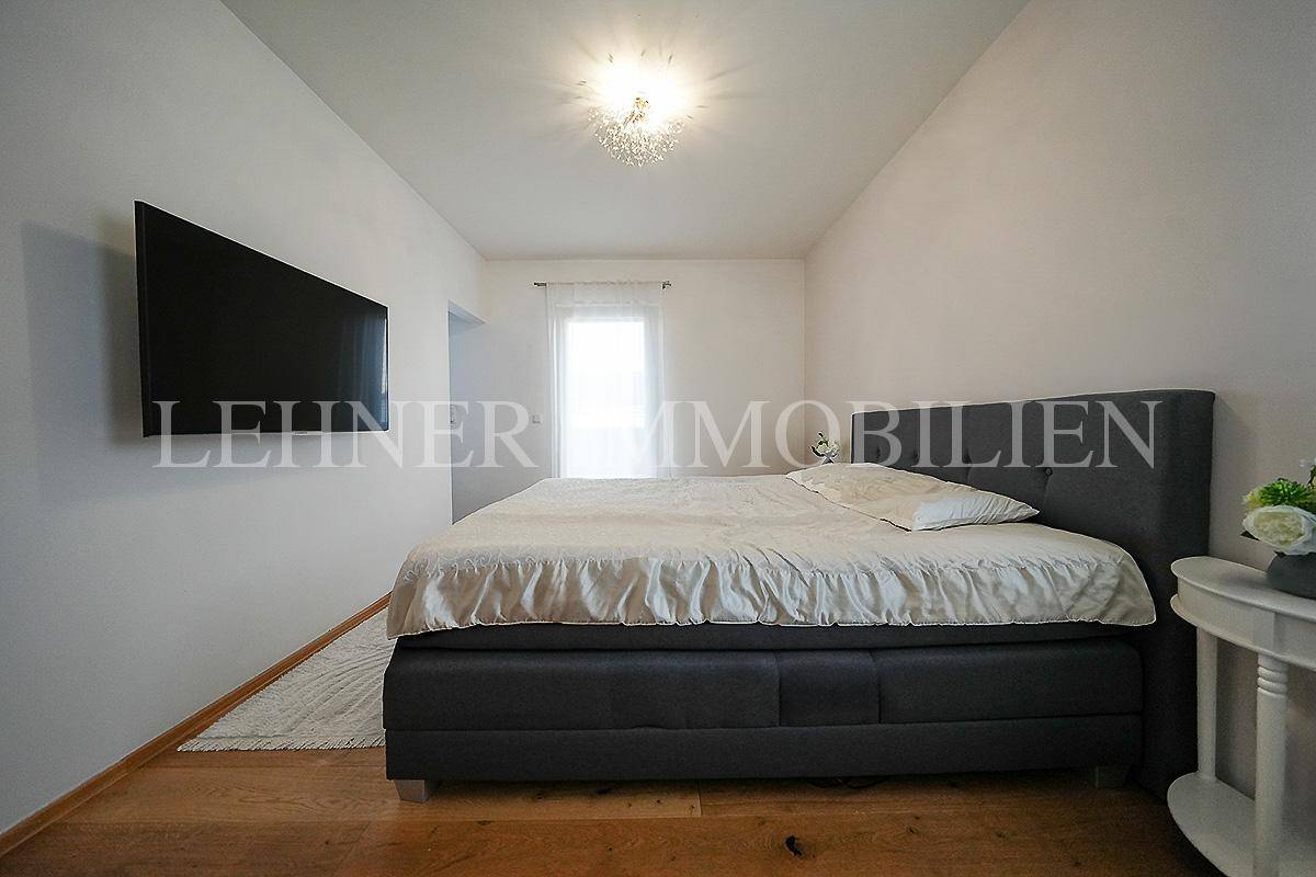 Schlafzimmer mit Holzboden, großem Bett und einem an der Wand montierten Fernseher.