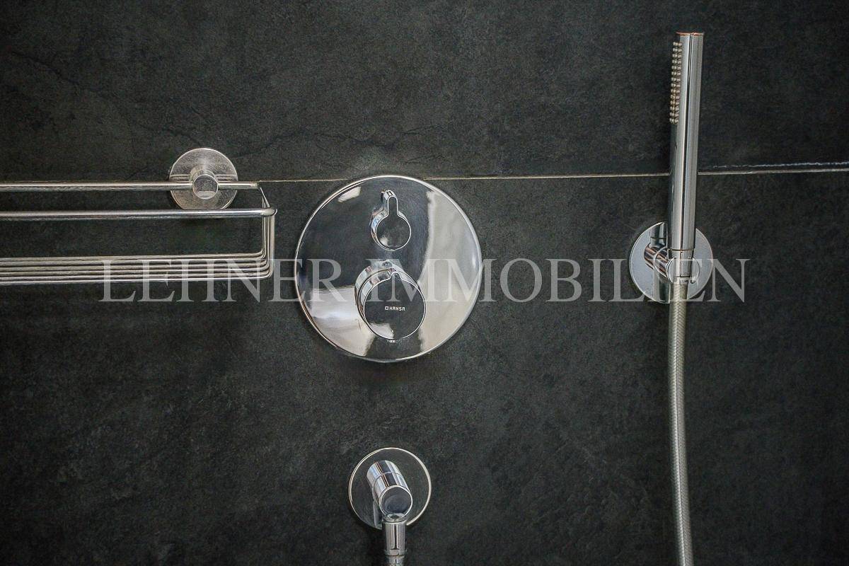 Detailaufnahme der modernen Duscharmaturen an der dunklen Wand im Badezimmer.