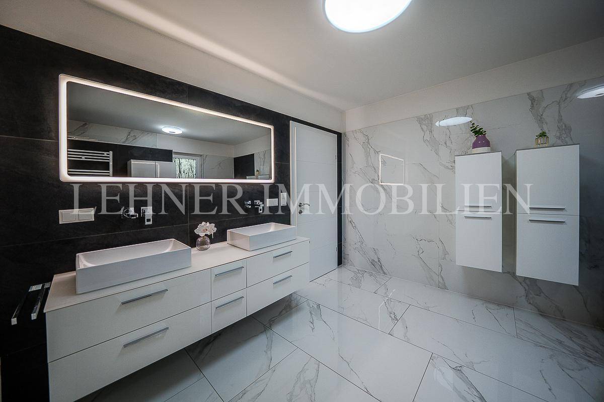 Modernes Badezimmer mit Doppelwaschbecken, beleuchtetem Spiegel und Marmorfliesen.